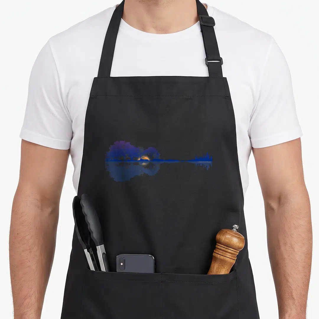 Guitar symphony lover apron - Guitar silhouette formed by purple and blue trees, orange sun, and city skyline — shown on a black cotton canvas apron against a white background