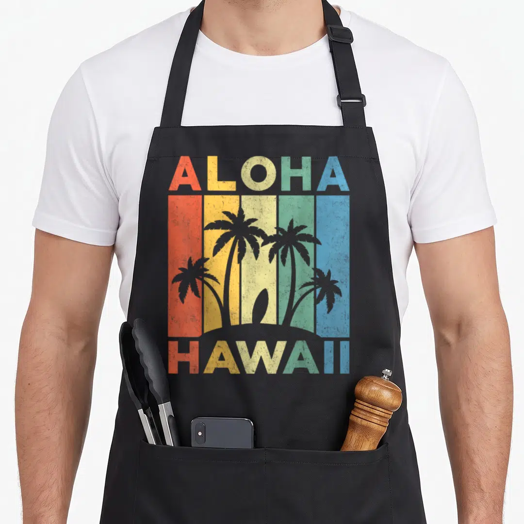 Hawaii kitchen island apron - Retro ALOHA HAWAII text with palm tree silhouettes over five colored vertical stripes — shown on a black cotton canvas apron against a white background