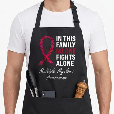 Myeloma family aprons - Heart-formed ribbon and IN THIS FAMILY NO ONE FIGHTS ALONE text for Multiple Myeloma — shown on a black cotton canvas apron against a white background