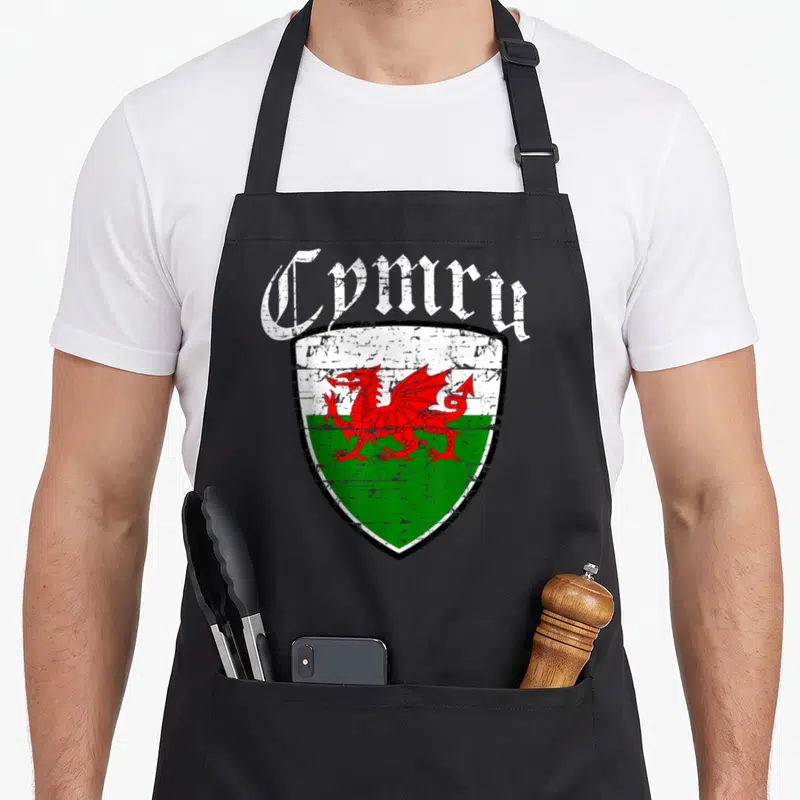 Cymru welsh apron - Distressed red dragon on white and green shield with arched Cymru text — shown on a black cotton canvas apron against a white background