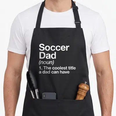 Soccer sports dad apron - White stacked text reading Soccer Dad noun definition on grey background — shown on a black cotton canvas apron against a white background