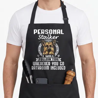 German christmas apron - German Shepherd head in white circle with Personal Stalker I Will Follow You Wherever You Go — shown on a black cotton canvas apron against a white background
