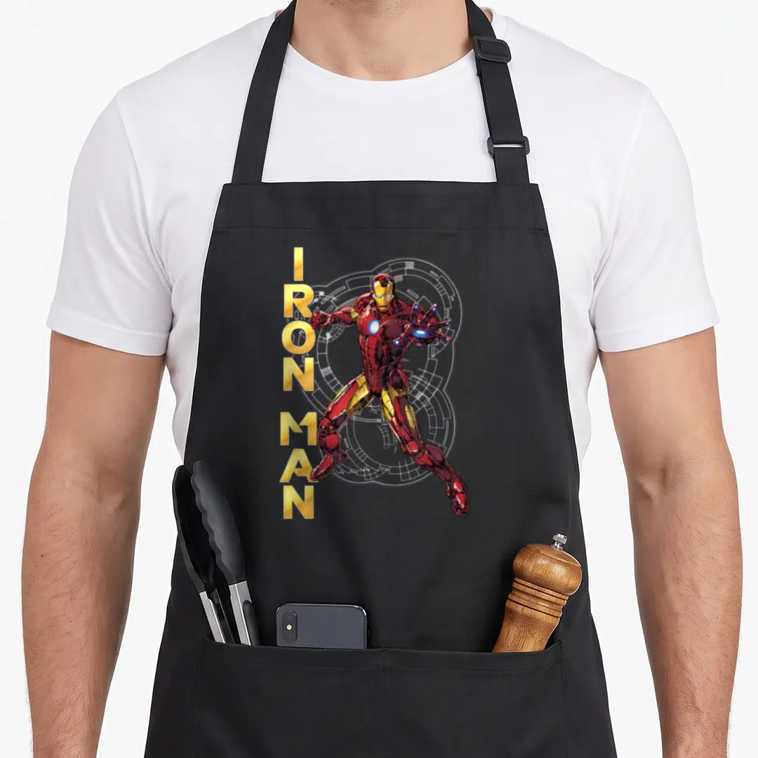 Assemble ironman apron - Vertical gold IRON MAN text beside red and gold armored figure with white circuitry background — shown on a black cotton canvas apron against a white background