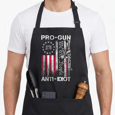 Anti 2nd apron - Distressed flag rifle Pro Gun Anti Idiot We the People 1776 text — shown on a black cotton canvas apron against a white background