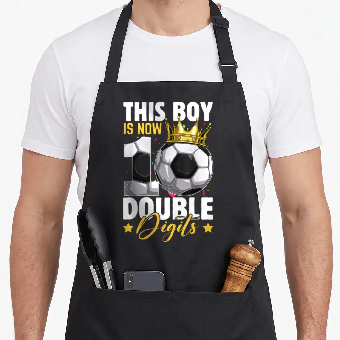 Digit soccer birthday apron - Crowned soccer ball next to number 10 with THIS BOY IS NOW DOUBLE Digits text — shown on a black cotton canvas apron against a white background