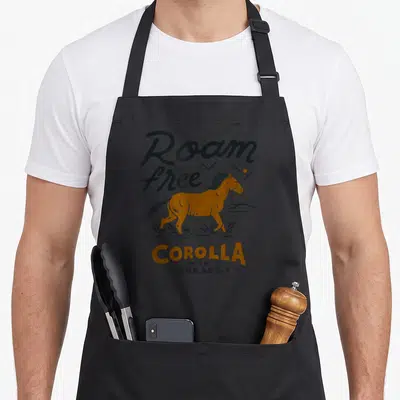 Corolla horse apron - Orange horse running through waves under Roam free text on grey background — shown on a black cotton canvas apron against a white background