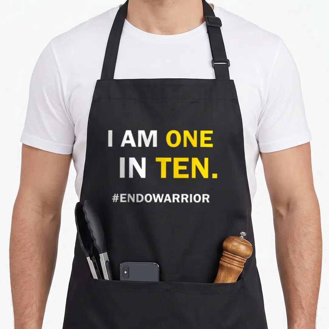 Funny endometriosis awareness apron - White and yellow text reading I AM ONE IN TEN and #ENDOWARRIOR stacked vertically — shown on a black cotton canvas apron against a white background