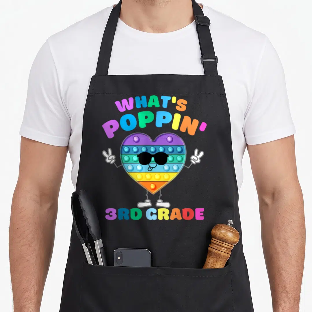 3rd fidget apron - Rainbow pop-it heart with sunglasses and 3rd grade text — shown on a black cotton canvas apron against a white background