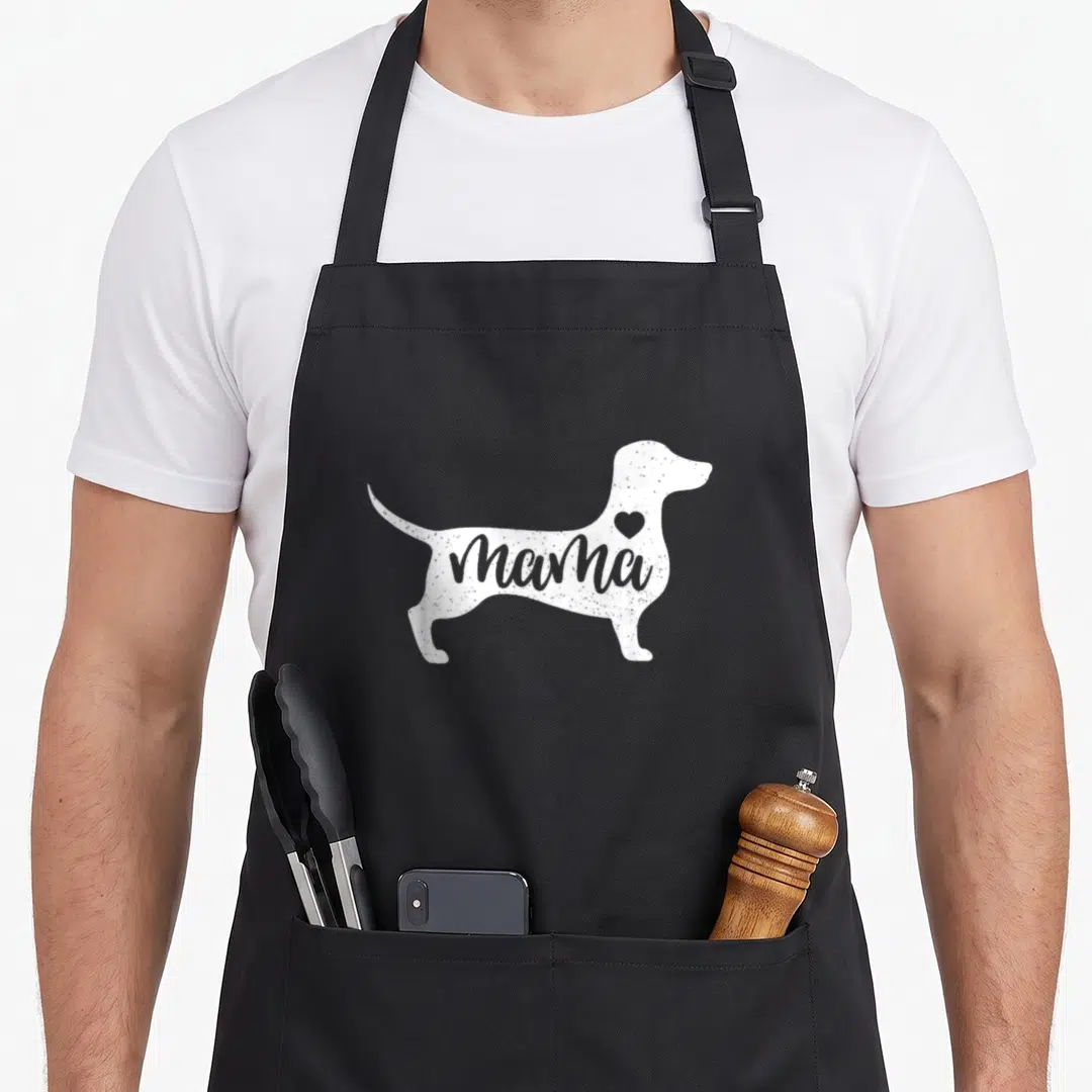 Dachshund mother's apron - White dachshund silhouette containing the word mama and a small heart on the shoulder — shown on a black cotton canvas apron against a white background
