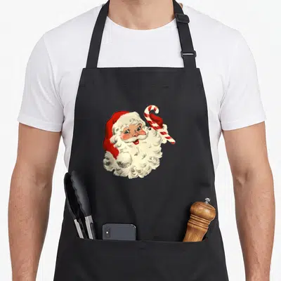 Claus candy cane apron - Vintage Santa Claus head holding red and white candy cane retro illustration — shown on a black cotton canvas apron against a white background