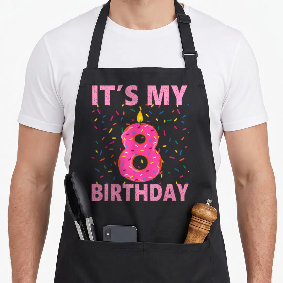 Sweet donut apron - Pink number 8 donut with candle and IT'S MY BIRTHDAY text surrounded by sprinkles — shown on a black cotton canvas apron against a white background