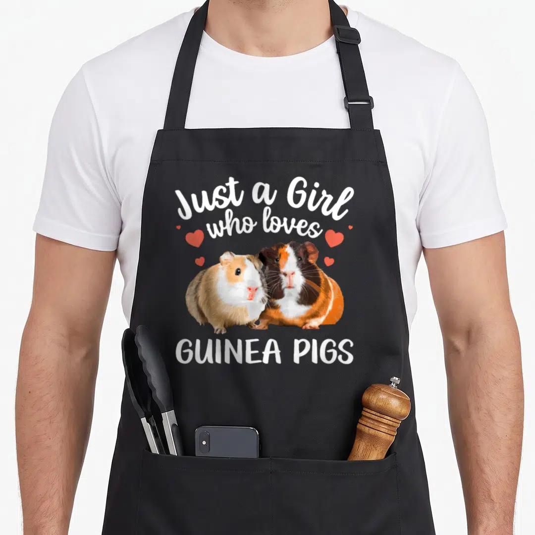 Clothe guinea lover apron - Two cartoon guinea pigs in white brown orange and red with scattered red hearts and printed — shown on a black cotton canvas apron against a white background