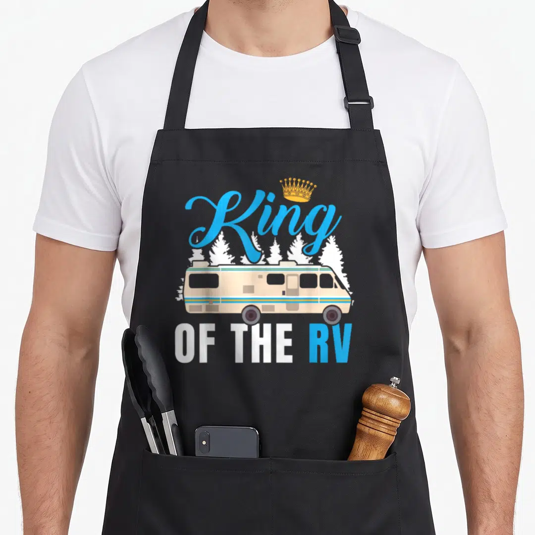 Owner king apron - Beige RV illustration with blue King OF THE RV text and golden crown graphic — shown on a black cotton canvas apron against a white background