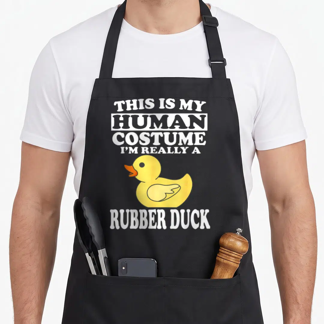Human rubber apron - Yellow cartoon duck with orange beak surrounded by white text saying THIS IS MY HUMAN COSTUME I'M — shown on a black cotton canvas apron against a white background