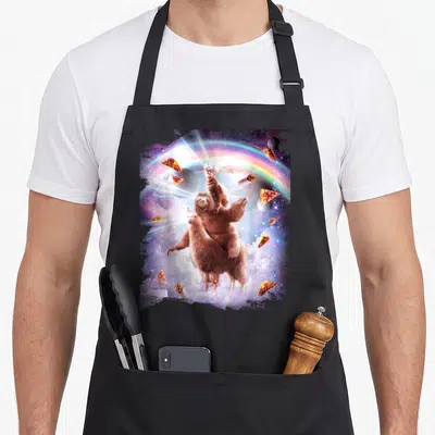 Laser space cat apron - Cat sloth llama stack in space with laser beams, pizza, tacos, rainbow, and clouds — shown on a black cotton canvas apron against a white background