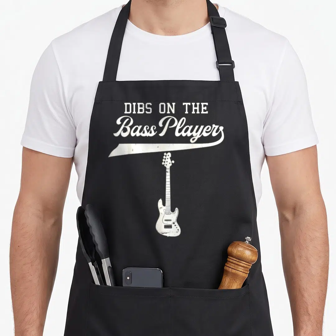Dib double apron - Distressed white text DIBS ON THE Bass Player above a vertical bass guitar illustration — shown on a black cotton canvas apron against a white background