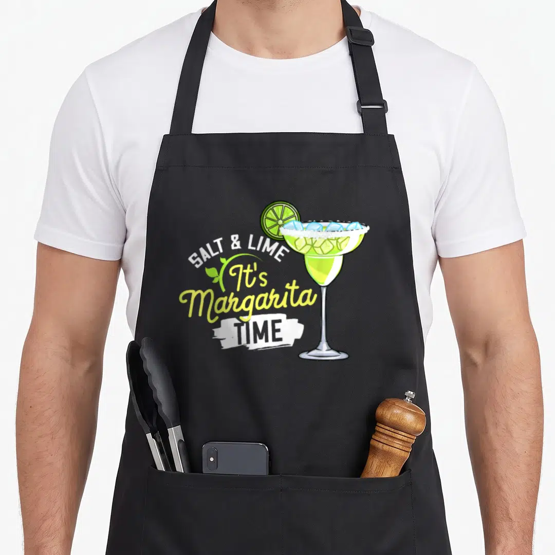Margarita limes apron - Cartoon margarita glass with ice and lime slice next to stacked text reading SALT & LIME It's — shown on a black cotton canvas apron against a white background