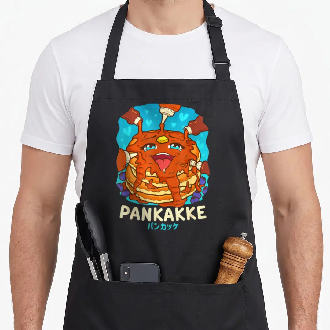 Cheeky kawaii apron - Stack of pancakes with face and syrup bottles on blue background with PANKAKKE text — shown on a black cotton canvas apron against a white background