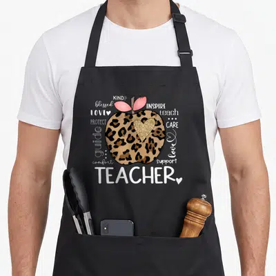 Teacher apple apron - Leopard print apple with gold heart surrounded by teacher appreciation words — shown on a black cotton canvas apron against a white background