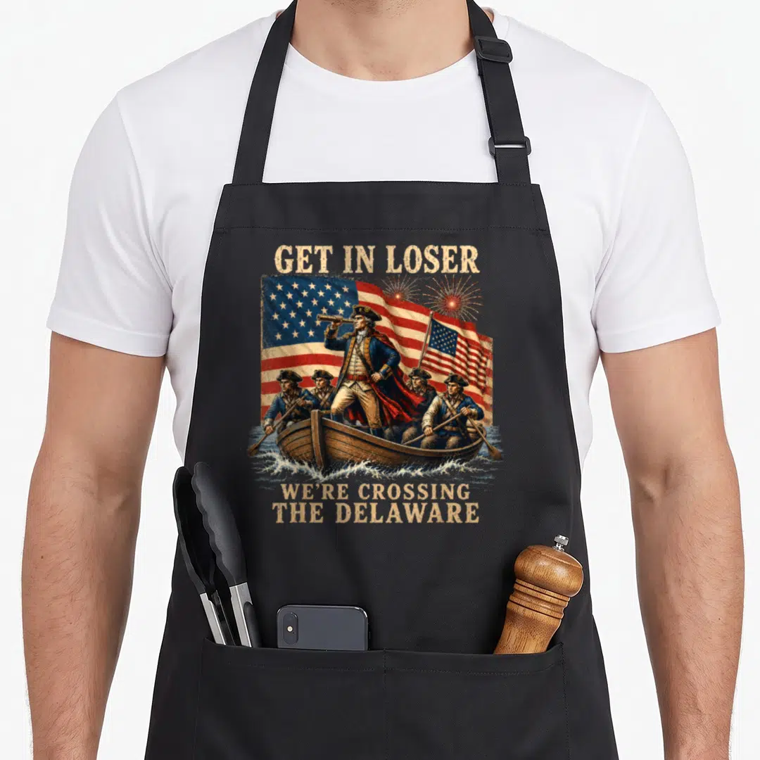 Crossing get loser apron - George Washington in a boat with men, flag, fireworks, and text GET IN LOSER WE'RE CROSSING — shown on a black cotton canvas apron against a white background