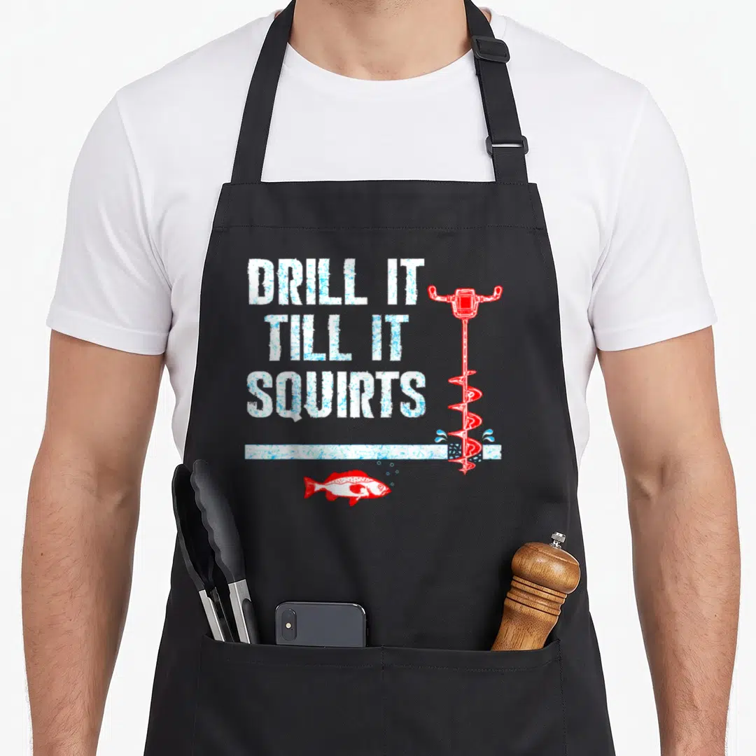 Drill fishing aprons - Distressed white text DRILL IT TILL IT SQUIRTS beside red ice auger and red fish under white line — shown on a black cotton canvas apron against a white background