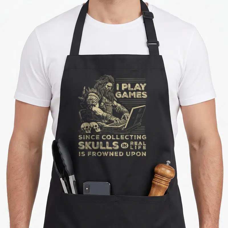Gaming skull apron - Tan line-art warrior typing on laptop beside two skulls with sarcastic gaming quote — shown on a black cotton canvas apron against a white background