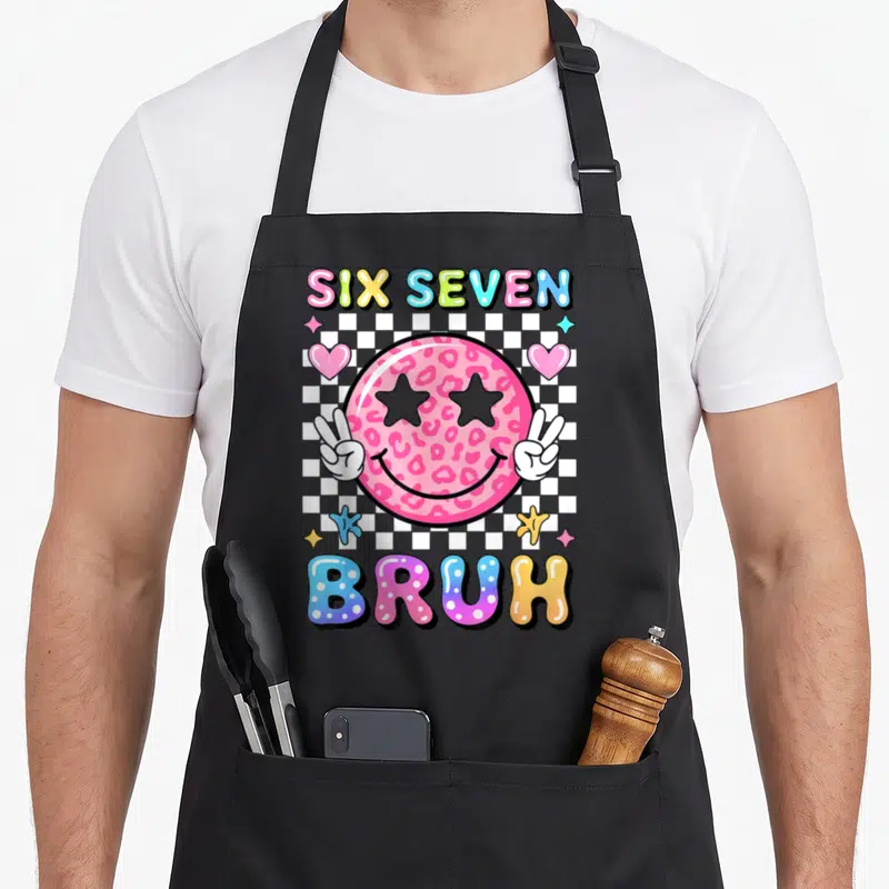 Face meme apron - Pink leopard print smiley face with star eyes and peace signs over checkerboard with SIX SEVEN BRUH — shown on a black cotton canvas apron against a white background