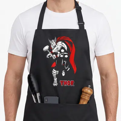 Hammer comics apron - Thor swinging hammer in red and white comic style with THE MIGHTY THOR text — shown on a black cotton canvas apron against a white background