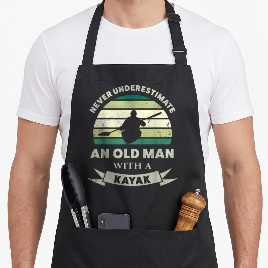 Funny kayak canoeing apron - Distressed retro sun with striped grey green yellow bands framing kayaker silhouette — shown on a black cotton canvas apron against a white background