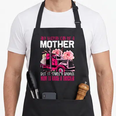 Badass truck apron - Pink semi-truck surrounded by roses with text honoring trucker mothers — shown on a black cotton canvas apron against a white background