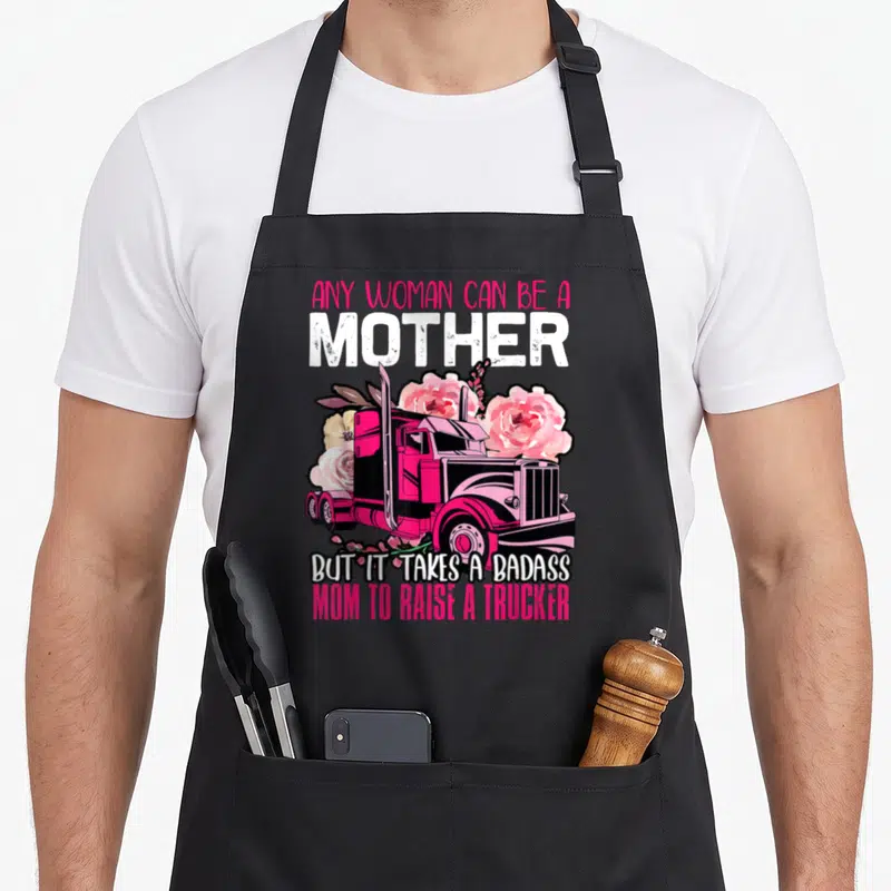 Badass truck apron - Pink semi-truck surrounded by roses with text honoring trucker mothers — shown on a black cotton canvas apron against a white background