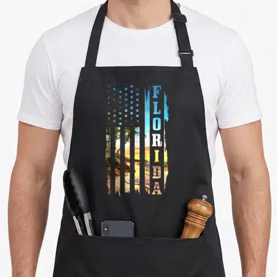 Beach american flag apron - Distressed USA flag with beach sunset stripes and vertical FLORIDA text — shown on a black cotton canvas apron against a white background