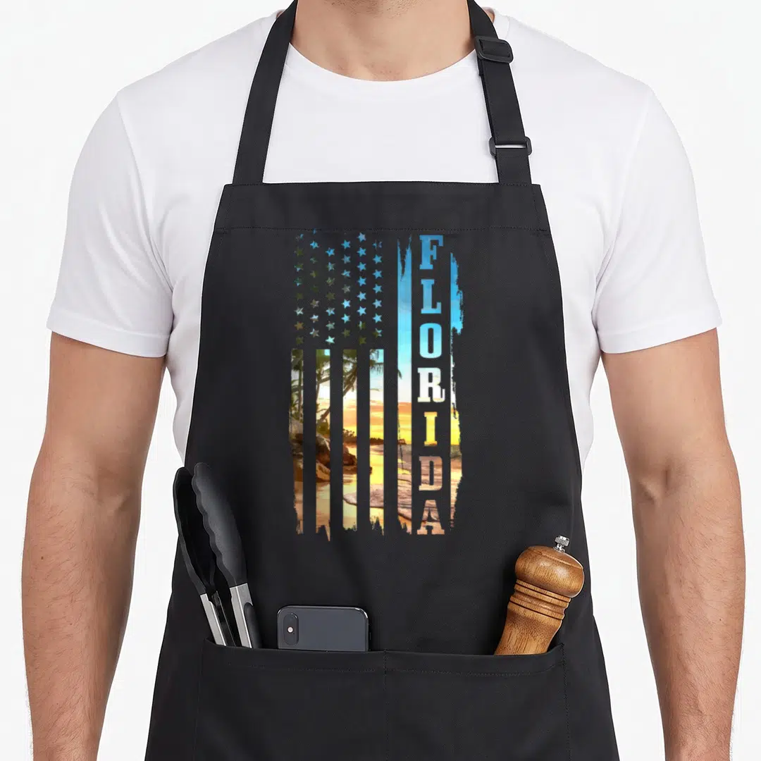 Beach american flag apron - Distressed USA flag with beach sunset stripes and vertical FLORIDA text — shown on a black cotton canvas apron against a white background