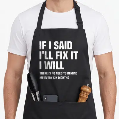 Mechanic fix handyman apron - White stacked text reading IF I SAID I'll FIX IT on grey background — shown on a black cotton canvas apron against a white background