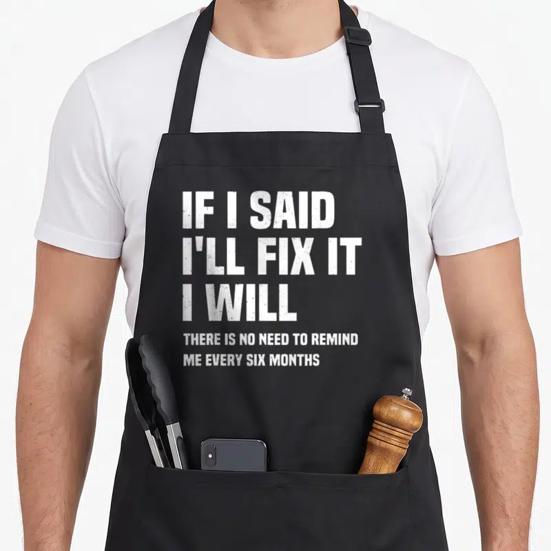 Mechanic fix handyman apron - White stacked text reading IF I SAID I'll FIX IT on grey background — shown on a black cotton canvas apron against a white background