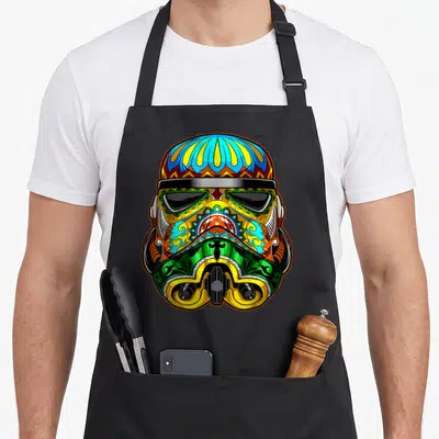 Ornate sugar skull apron - Cartoon stormtrooper helmet decorated with blue yellow green red and orange sugar skull — shown on a black cotton canvas apron against a white background