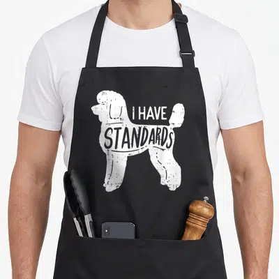 Pet standard size of apron - White distressed poodle silhouette with I HAVE STANDARDS text — shown on a black cotton canvas apron against a white background