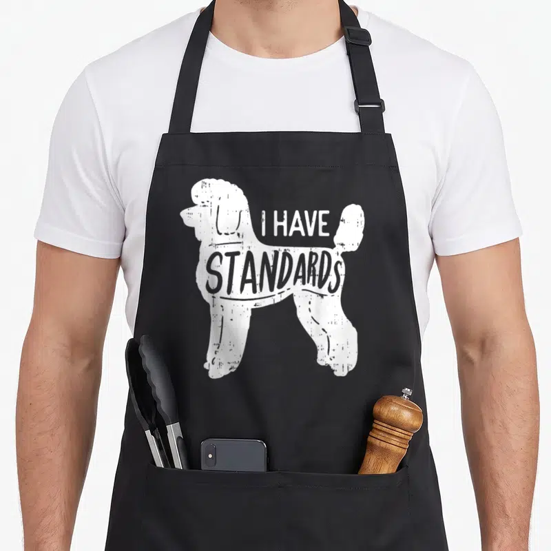 Pet standard size of apron - White distressed poodle silhouette with I HAVE STANDARDS text — shown on a black cotton canvas apron against a white background
