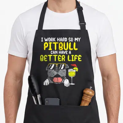 Hard pitbull dog apron - Cartoon grey pitbull with yellow sunglasses and cocktail glass below stacked white and yellow — shown on a black cotton canvas apron against a white background