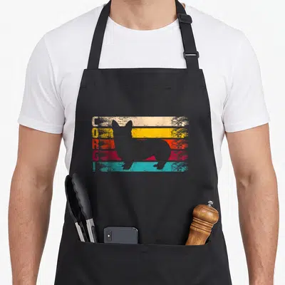 Silhouette corgi apron - Grey corgi silhouette over five colored stripes with vertical CORGI text — shown on a black cotton canvas apron against a white background
