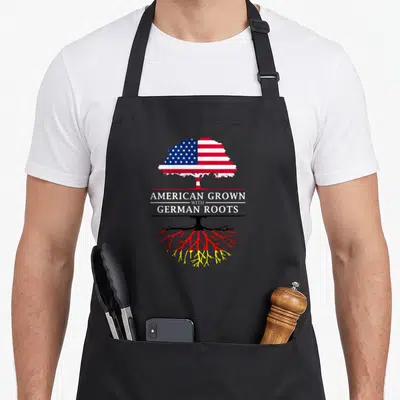 Grown german apron - Tree with US flag canopy and German colored roots text American Grown with German Roots — shown on a black cotton canvas apron against a white background