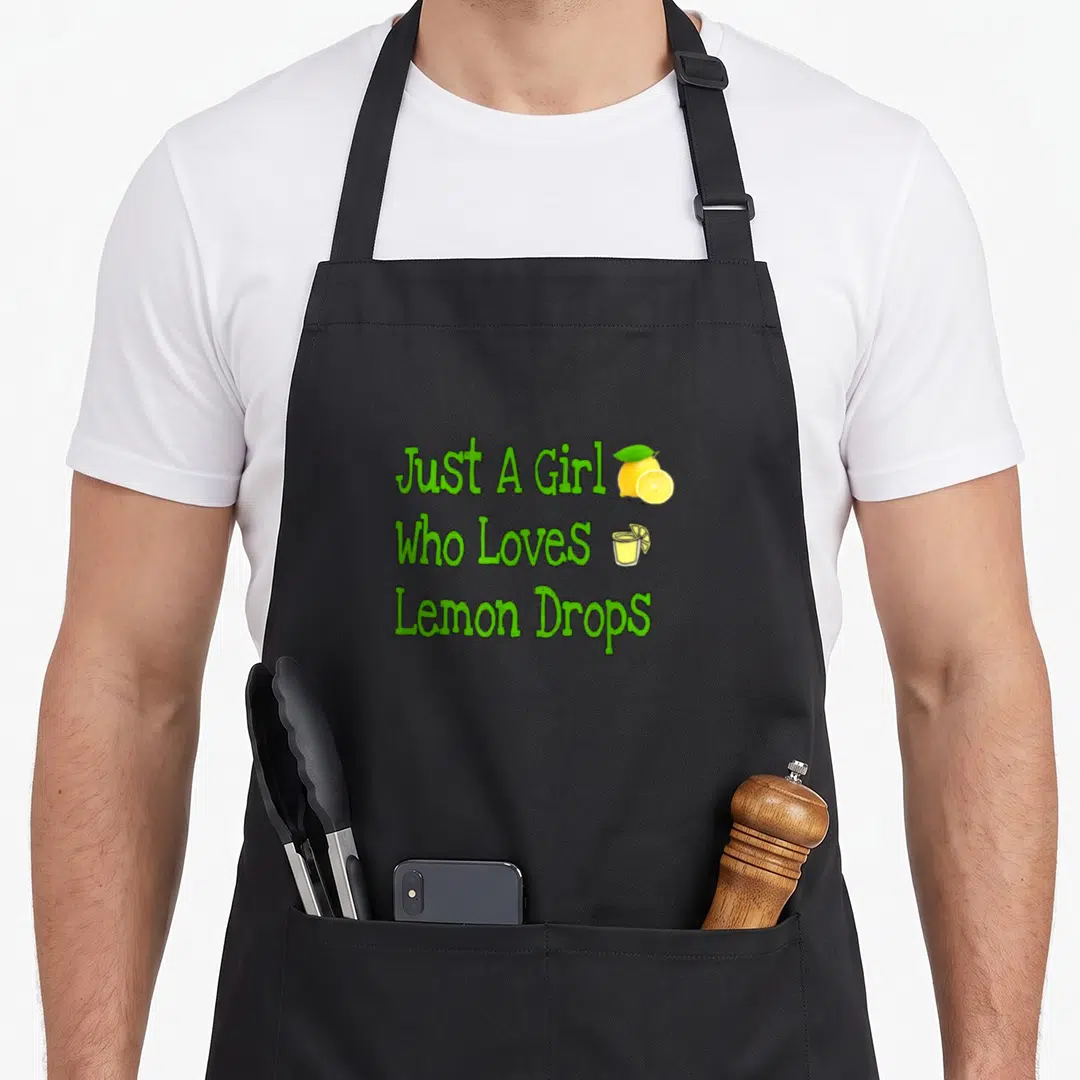 Cute drop for love and lemons apron - Green text Just A Girl Who Loves Lemon Drops with yellow lemon and cocktail glass — shown on a black cotton canvas apron against a white background