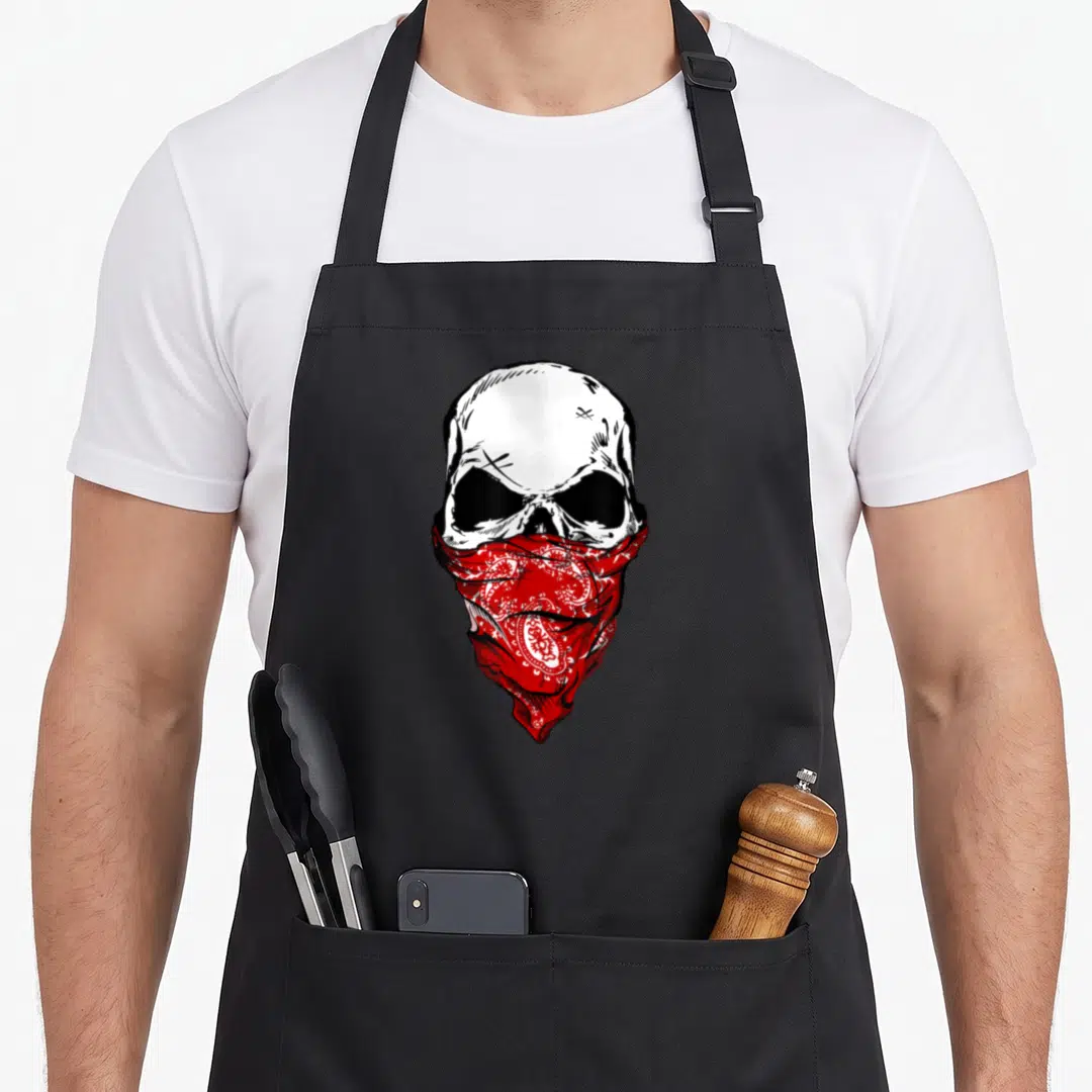 Fearless skeleton apron - Realistic white skull wearing a red paisley bandana mask over the jaw — shown on a black cotton canvas apron against a white background