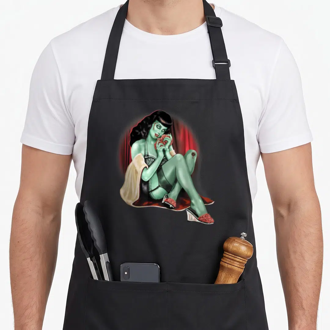 Model pin up apron - Green woman in black lingerie holding red heart against red curtains wearing cream robe — shown on a black cotton canvas apron against a white background