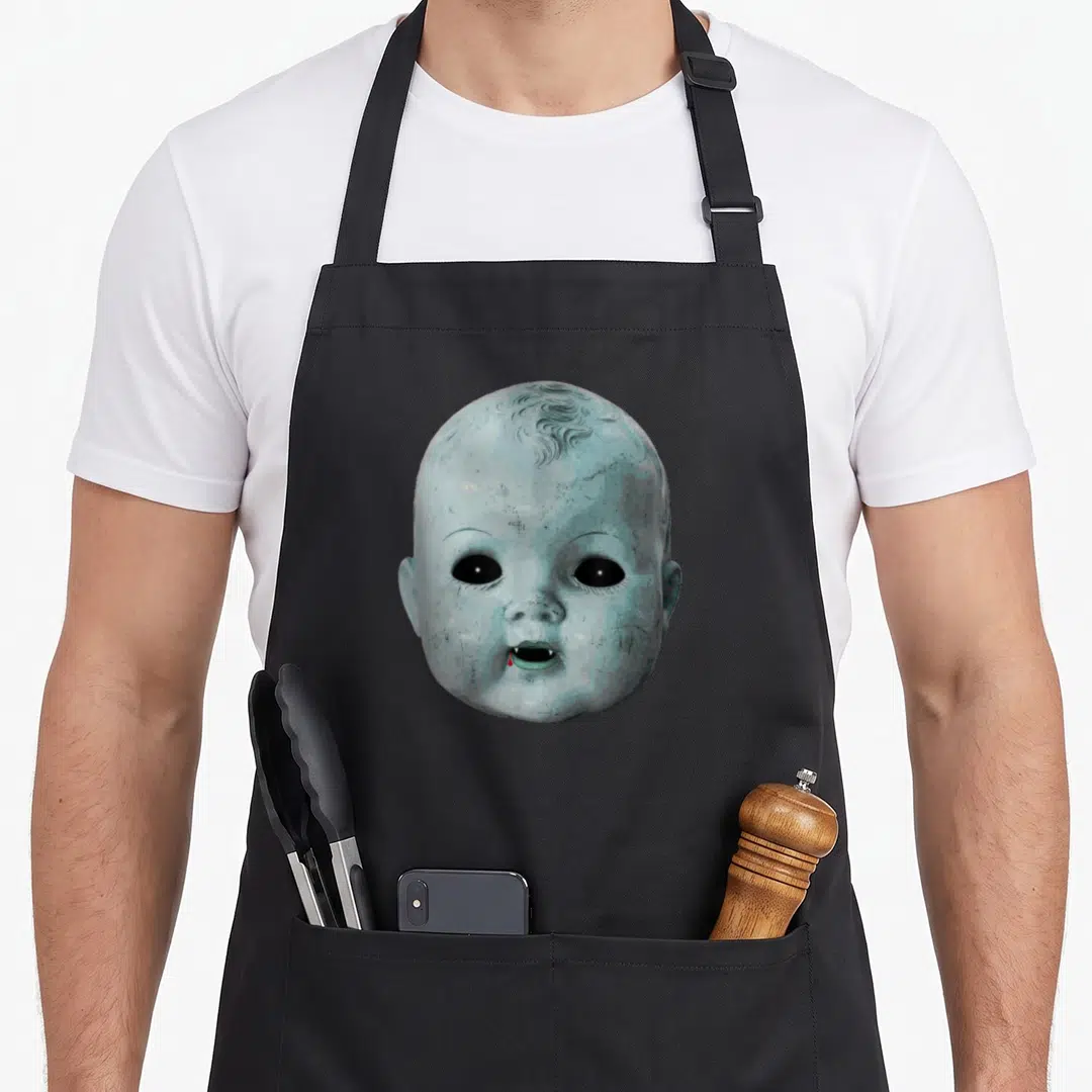 Creepy halloween apron - Realistic pale blue baby head with black eyes, fangs, and a red drop — shown on a black cotton canvas apron against a white background