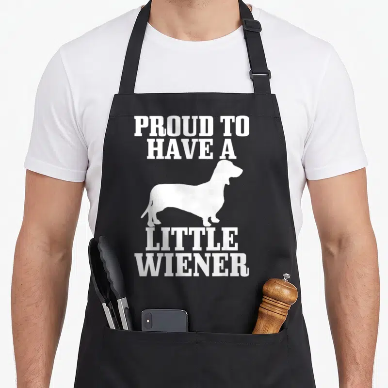 Proud dog wiener apron - White dachshund silhouette with PROUD TO HAVE A LITTLE WIENER text stacked above and below — shown on a black cotton canvas apron against a white background