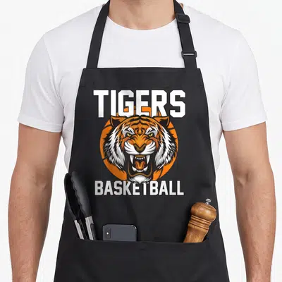 Tiger crew apron - Cartoon tiger head over orange basketball with TIGERS BASKETBALL text in white and black — shown on a black cotton canvas apron against a white background