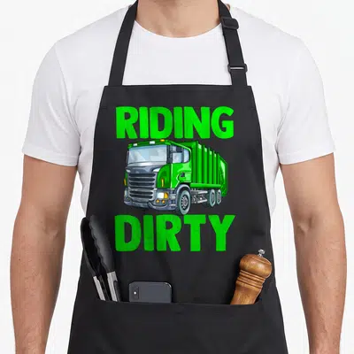 Recycling the dirty apron - Green garbage truck illustration with RIDING DIRTY text in bold letters — shown on a black cotton canvas apron against a white background