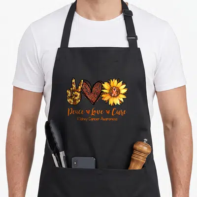 Peace daisy apron - Peace sign heart sunflower with orange yellow brown patterns and awareness text — shown on a black cotton canvas apron against a white background