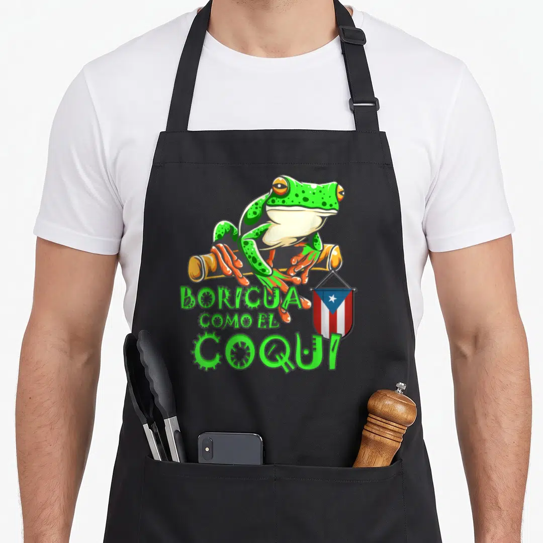 Rican frog aprons - Cartoon frog perched on branch with BORICUA COMO EL COQUI text and Puerto Rican flag — shown on a black cotton canvas apron against a white background